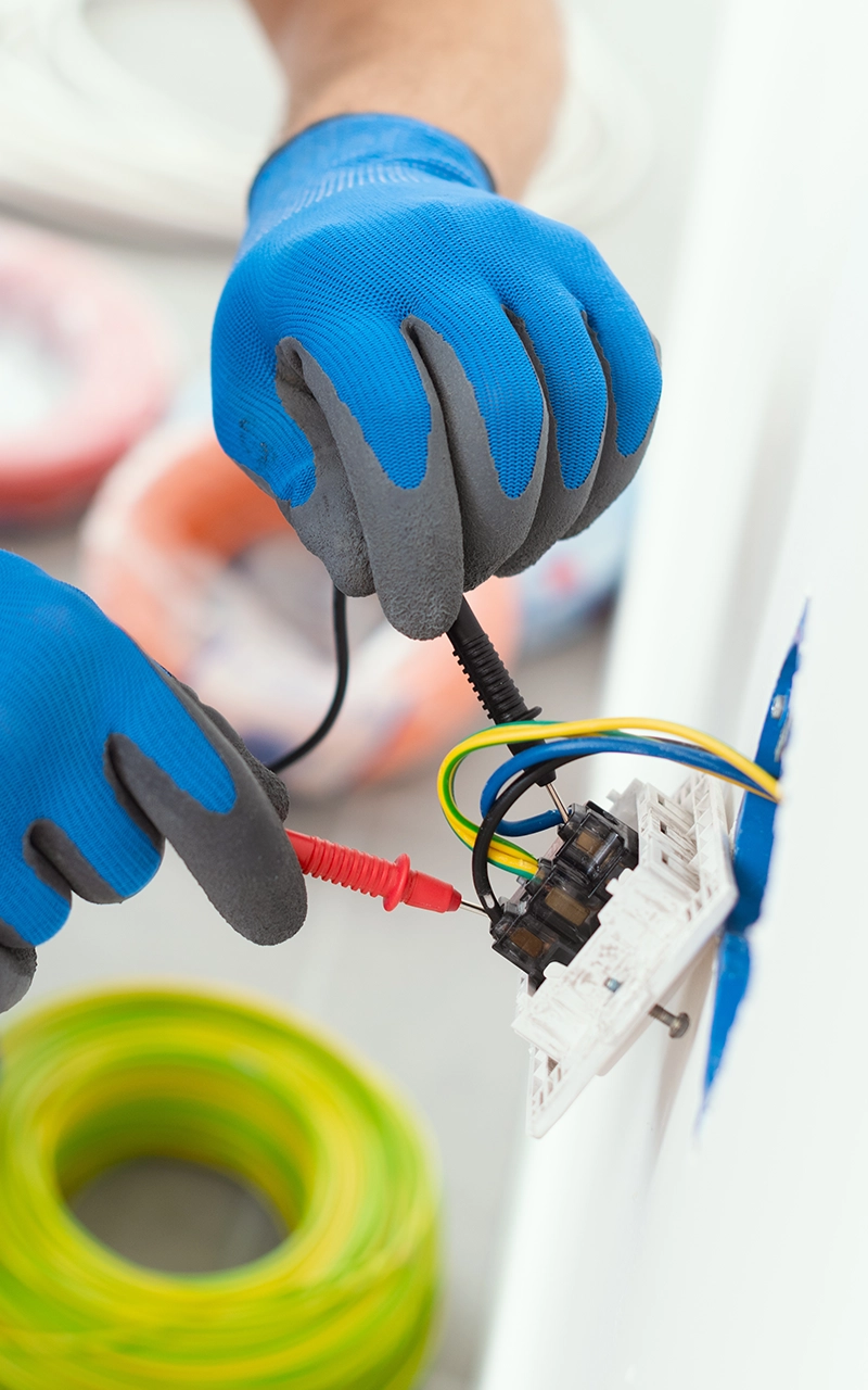 Électricien effectuant des raccordements de câbles avec des gants de sécurité.