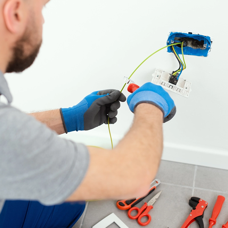 Électricien installant une prise électrique murale.