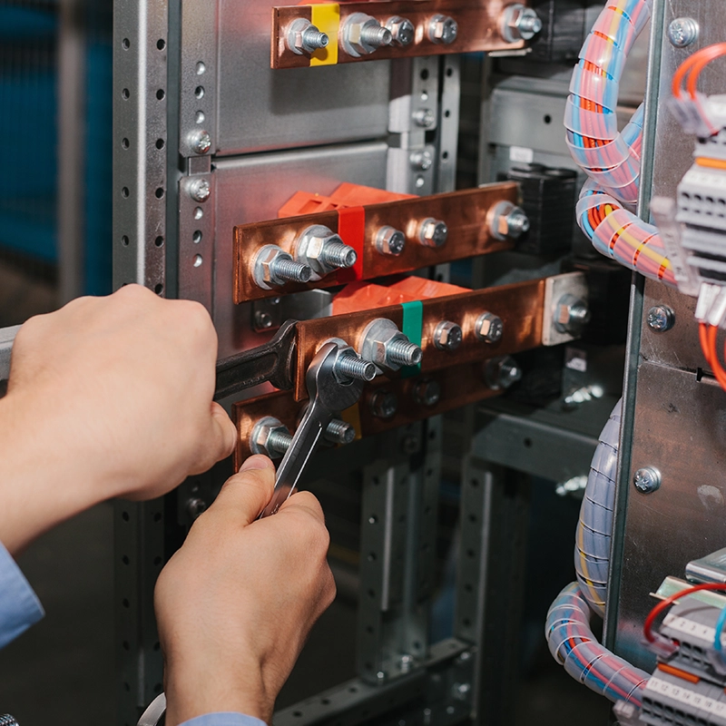 Électricien utilisant une clé pour ajuster des connexions dans un tableau électrique.