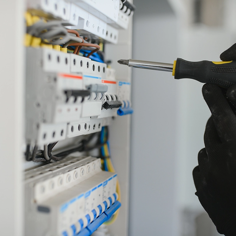 Technicien électricien utilisant un tournevis pour vérifier un tableau électrique.